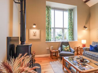 A living room with a wood stove sofa armchair coffee table and window with green curtains at Old Howgate Barn Outgate near Hawkshead