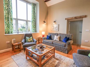 A living room with a striped sofa, armchairs, wooden coffee table, patterned curtains, and wall art at Old Howgate Barn Outgate near Hawkshead