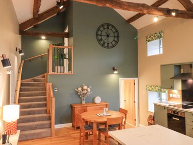 A kitchen and dining area with a wooden staircase and a large wall clock at Old Howgate Barn Outgate near Hawkshead