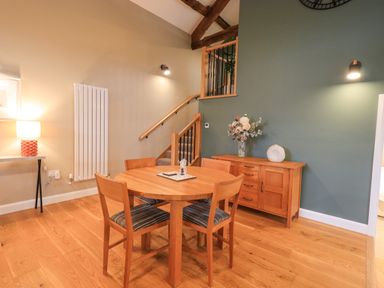 A dining area with a round wooden table and four chairs next to a staircase and a wooden sideboard with flowers at Old Howgate Barn Outgate near Hawkshead