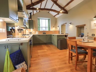 A kitchen with green cabinets wooden beams and a wooden dining table at Old Howgate Barn Outgate near Hawkshead