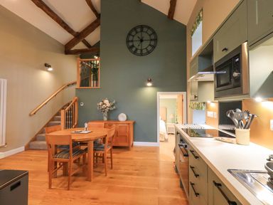 A kitchen and dining area with wooden table and chairs a wall clock and stairs at Old Howgate Barn Outgate near Hawkshead