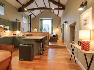 A kitchen and living area with wooden beams an island with stools and a window at Old Howgate Barn Outgate near Hawkshead