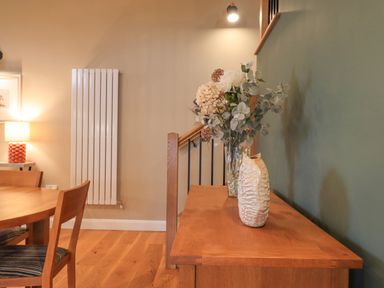 A wooden dining table with chairs a sideboard with a vase and flowers against a green wall at Old Howgate Barn Outgate near Hawkshead