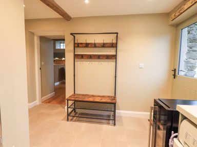A hallway with a wooden bench and coat rack near a door with a window at Old Howgate Barn Outgate near Hawkshead