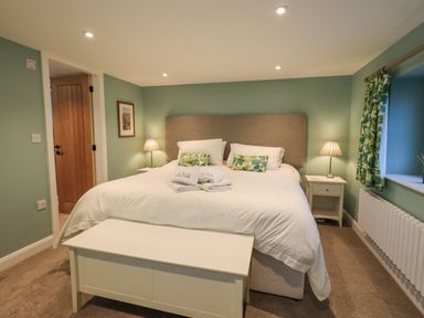 A bedroom with a large bed lamps on bedside tables and a window with curtains at Old Howgate Barn Outgate near Hawkshead