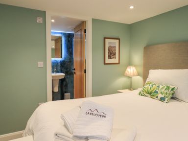 A bedroom with a bed a bedside table with lamp framed picture on wall and an open door to an ensuite bathroom at Old Howgate Barn Outgate near Hawkshead