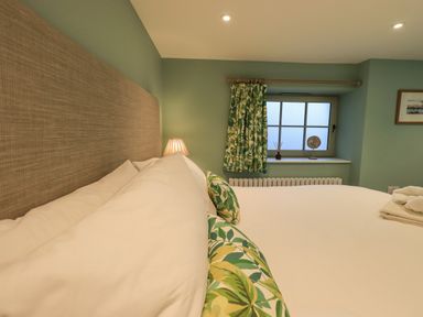 A bedroom with a bed white bedding floral pillows green wall curtains and a window at Old Howgate Barn Outgate near Hawkshead