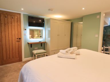 A bedroom with a bed with folded towels wardrobe a wall-mounted tv and a door at Old Howgate Barn Outgate near Hawkshead