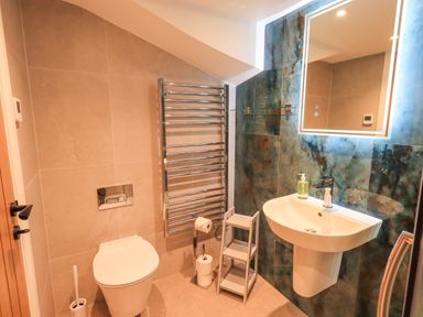 A bathroom with a toilet, sink with soap dispenser, towel radiator, mirror, and wall tiles at Old Howgate Barn Outgate near Hawkshead