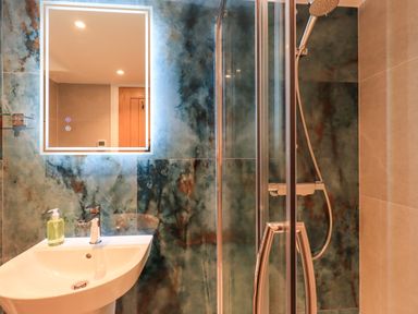 A bathroom with a sink and liquid soap dispenser a shower area with glass doors and a rainfall showerhead at Old Howgate Barn Outgate near Hawkshead
