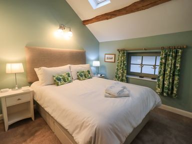 A bedroom with a large bed bedside tables lamps and a window with green patterned curtains at Old Howgate Barn Outgate near Hawkshead