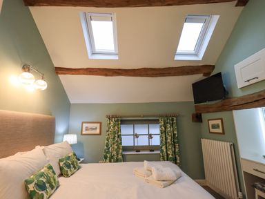 A bedroom with a bed white linens green patterned cushions and curtains skylights and wooden beams at Old Howgate Barn Outgate near Hawkshead