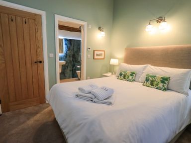 A bedroom with a large bed white bedding green patterned pillows lamps and an en suite bathroom at Old Howgate Barn Outgate near Hawkshead