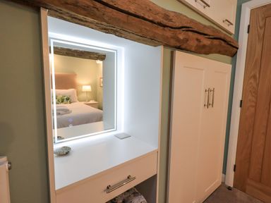 A dressing table with an illuminated mirror next to a white wardrobe and a wooden door at Old Howgate Barn Outgate near Hawkshead