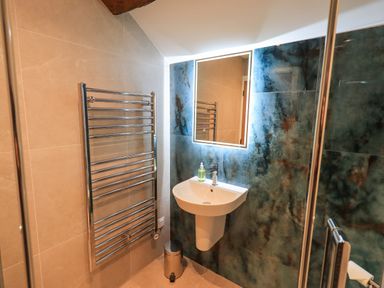 A bathroom with a wall-mounted sink soap dispenser illuminated mirror towel radiator and waste bin at Old Howgate Barn Outgate near Hawkshead