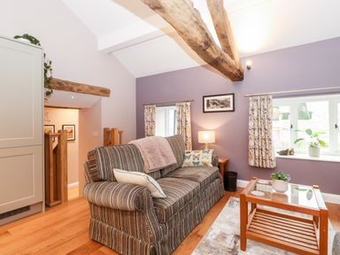 A sitting area with a striped sofa and wooden coffee table with plants and windows at Low Ashmead Cottage in Hawkshead