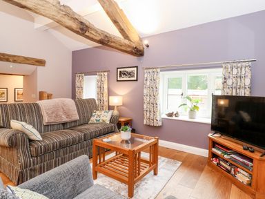 A living room with a striped sofa a wooden coffee table a television on a wooden stand and wooden ceiling beams at Low Ashmead Cottage in Hawkshead