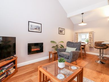 A living room with a television a glass coffee table a gray armchair and a dining area at Low Ashmead Cottage in Hawkshead