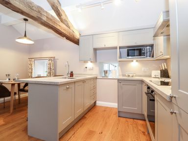 A kitchen with grey cabinets an island with a sink wooden ceiling beams and a dining area at Low Ashmead Cottage in Hawkshead