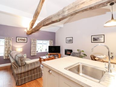 An open living area with a striped sofa a wooden coffee table a television on a stand and a kitchen island with a sink at Low Ashmead Cottage in Hawkshead