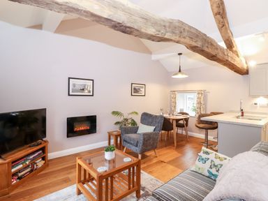 A living room with wooden beams dining table chairs TV and fireplace at Low Ashmead Cottage in Hawkshead