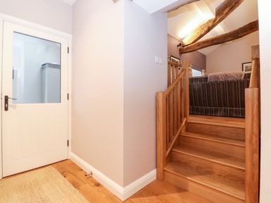 A wooden staircase leading to a room with a striped couch and visible wooden ceiling beams at Low Ashmead Cottage in Hawkshead