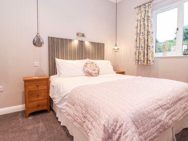 A bedroom with a double bed a striped headboard pink quilt bedside tables and a window with floral curtains at Low Ashmead Cottage in Hawkshead