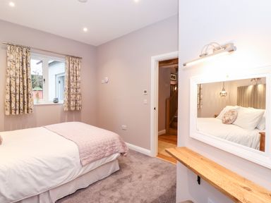A bedroom with a bed covered in white and pink quilt near a window with patterned curtains at Low Ashmead Cottage in Hawkshead