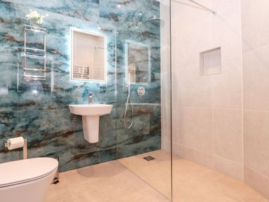 A bathroom with a toilet sink and walk in shower with blue and beige tiled walls at Low Ashmead Cottage in Hawkshead