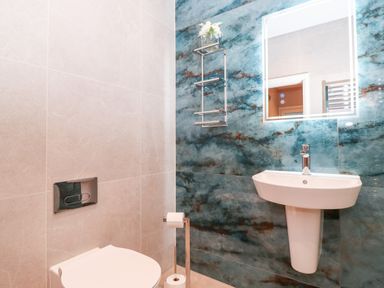 A bathroom with a white toilet and a white sink against blue and beige tiled walls at Low Ashmead Cottage in Hawkshead