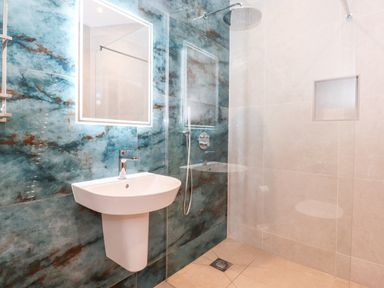 A bathroom with a wall-mounted sink a shower area with a rain shower head and a recessed shelf at Low Ashmead Cottage in Hawkshead