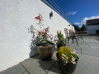 An outdoor patio with potted plants and metal chairs near a white textured wall at Low Ashmead Cottage in Hawkshead