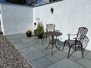 An outdoor patio area with two metal chairs a small round metal table and three potted plants against a white textured wall at Low Ashmead Cottage in Hawkshead