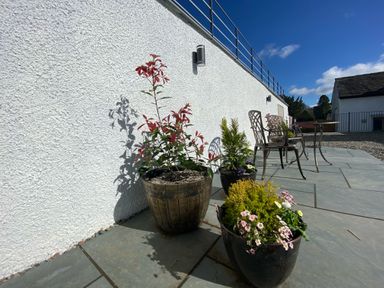 A patio with potted plants and metal chairs against a white wall at Low Ashmead Cottage in Hawkshead