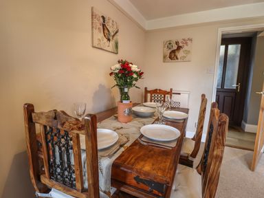 A dining room with a wooden table set for four with plates glasses flowers and a bottle at Rayside in Ullswater