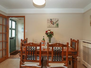 A dining room with a wooden table and chairs set with plates and glasses and a vase of flowers at Rayside in Ullswater