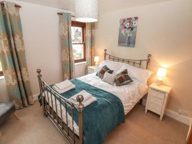 A bedroom with a metal bed frame bedside tables with lamps and floral curtains at Rayside in Ullswater
