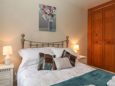 A bedroom with a metal bed frame a bed with pillows and cushions two bedside tables with lamps and a wooden wardrobe at Rayside in Ullswater