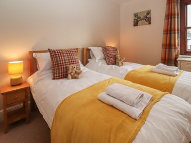 A bedroom with two single beds yellow throws and plaid pillows at Rayside in Ullswater