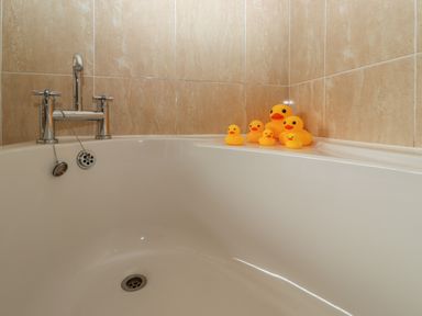 A bathtub with six rubber ducks on the edge and a silver faucet in a tiled bathroom at Rayside in Ullswater