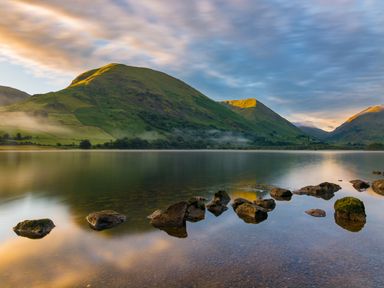 A lake with rocks in the water and green hills in the background at Rayside in Ullswater
