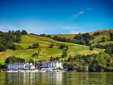 A marina with sailboats in front of white buildings and green hills at Rayside in Ullswater