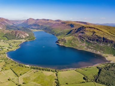 A large lake surrounded by green fields and mountains under a clear blue sky at Rayside in Ullswater