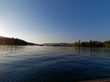 A lake with several boats on the water and trees on both shores at Rayside in Ullswater
