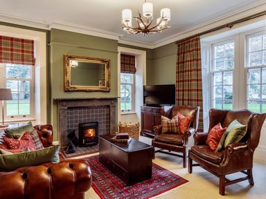 A living room with leather chairs a fireplace a television and plaid curtains at The Vicarage near Rosthwaite