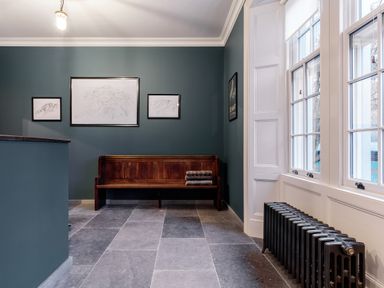 A hallway with a wooden bench stacked with blankets a radiator and three framed pictures on the wall at The Vicarage near Rosthwaite