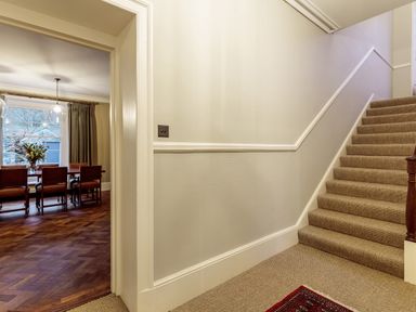 A staircase with carpet leading up and a dining room with a wooden table and chairs visible through a doorway at The Vicarage near Rosthwaite