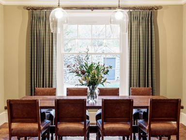 A dining room with a wooden table and leather chairs with flowers in a vase at The Vicarage near Rosthwaite