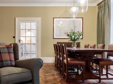 A dining room with a wooden table and leather chairs a vase with flowers and a glass door leading to a kitchen at The Vicarage near Rosthwaite